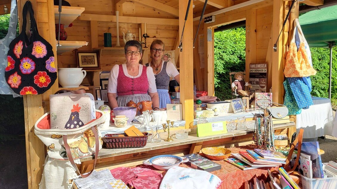 Der Holzstand vom Hospiz Ausseerland Hinterberg mit zwei ehrenamtlichen Mitarbeiterinnen. Selber tragen die Damen ein Dirndkleid und im Vordergrund sind die Verkaufsstücke ausgestellt.  | © Petra Kirchschlager