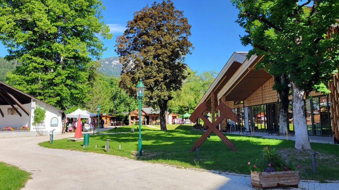 Rechts ist der Veranstaltungssaal Altaussee mit dem Cafe und auf der linken seite die Markstände vom Mark im Kurpark. Das Bergmannszeichen Hammer und Schlägel ist im Vordergrund zu sehen. | © Petra Kirchschlager