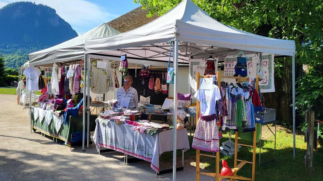 <p>Die trachtigen Kleidungsstücke der Familie Büttner werden unter einem weißen Zelt beim Markt in Kurpark Altaussee prästentiert. Im Hintergrund ist der Tressenstein zu sehen.</p> | © Petra Kirchschlager