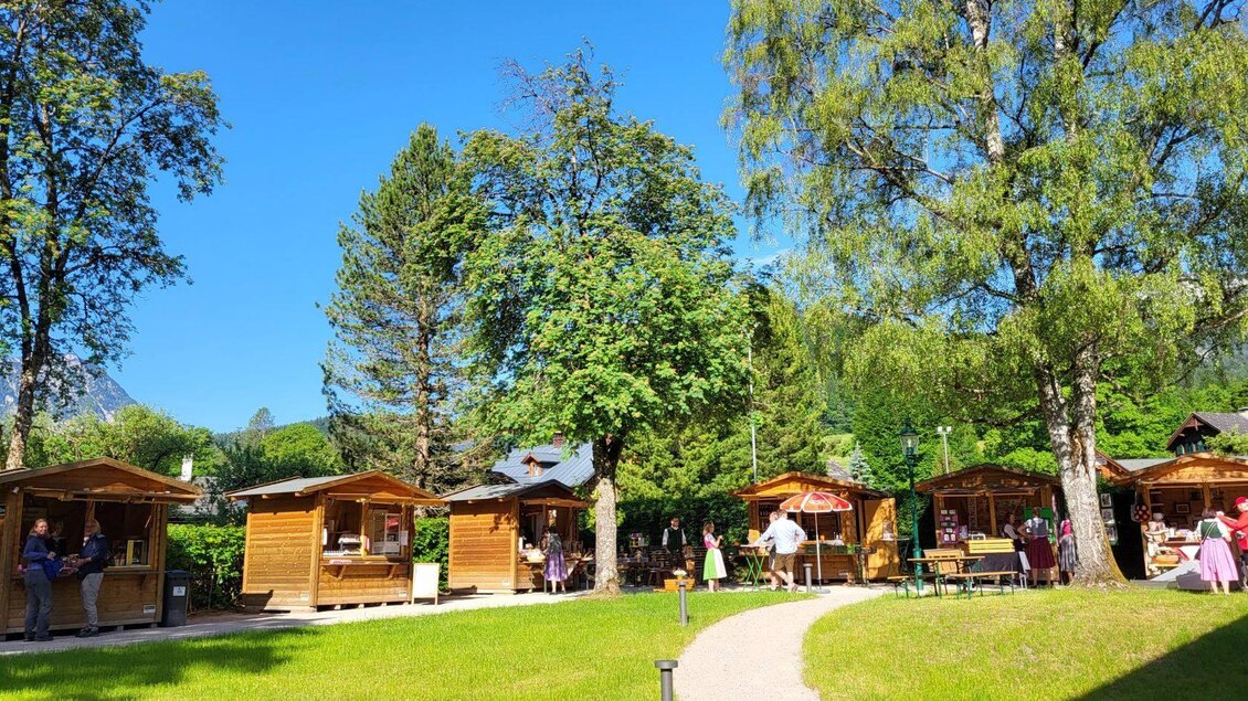 <p>Ein malerischer Markt im Kurpark Altaussee mit vielen Holzständen umgeben von üppigem Grün. Die Sonne scheint hell auf das Markttreiben.</p> | © Petra Kirchschlager