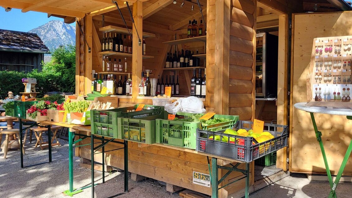 Ein kleiner Verkaufsstand aus Holz mit frischen Produkten. Es gibt Gemüse, Obst und Getränke, umgeben von einer schönen Landschaft. | © Petra Kirchschlager