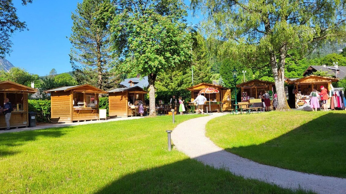 Im grünen Kurpark von Altaussee stehen die Holz-Verkaufs-Stände. Bei Sonnenschein erkunden die Besucher den Markt in Kurpark Altaussee. | © Petra Kirchschlager