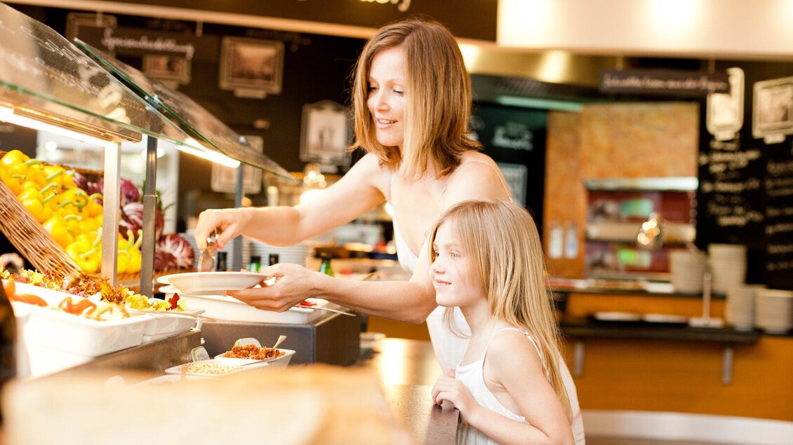 <p>Eine Frau und ein Mädchen stehen an einem Buffet und wählen Essen aus. Im Hintergrund sind frische Speisen und eine einladende Umgebung zu sehen. Marktrestaurant Thermenresort Loipersdorf in Bad Loipersdorf.</p> | © Thermenresort Loipersdorf