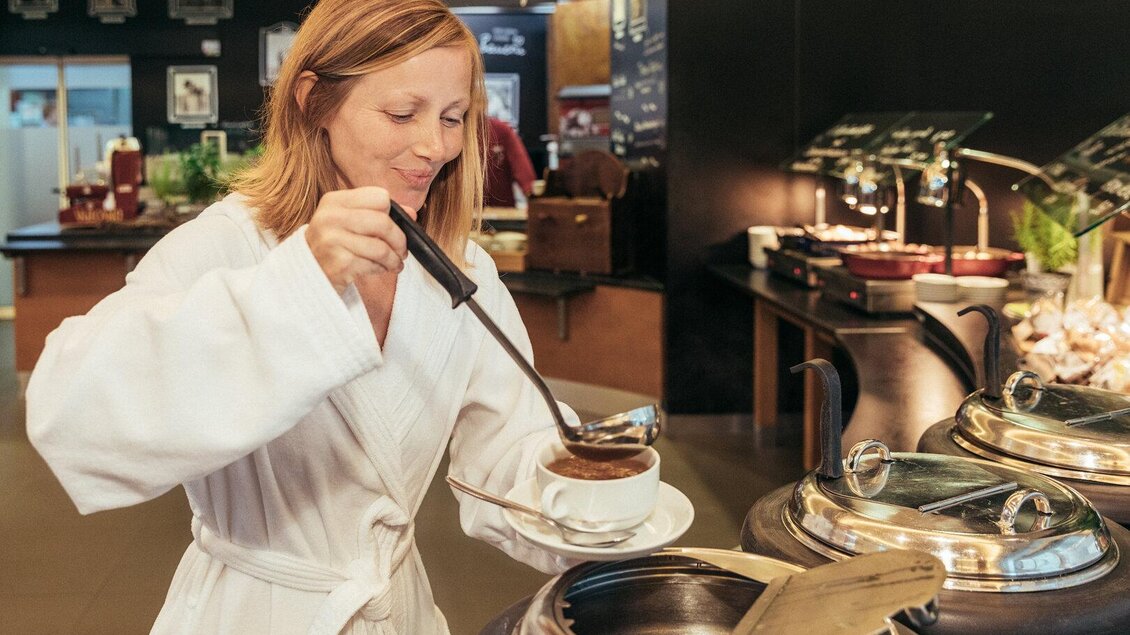 <p>Eine Frau in einem Bademantel serviert sich eine Tasse Kaffee an einem Buffet. Der Raum hat eine gemütliche Atmosphäre mit verschiedenen Speisen. Marktrestaurant Thermenresort Loipersdorf in Bad Loipersdorf.</p> | © Thermenresort Loipersdorf