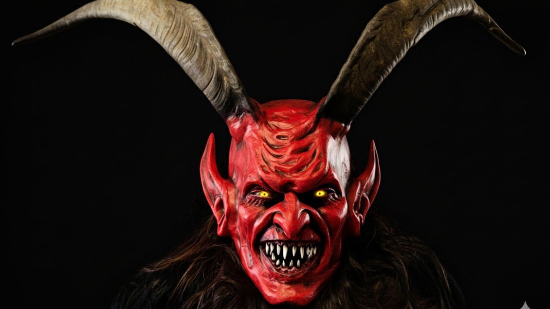 Eine gruselige Maske mit roten und schwarzen Farben, spitzen Ohren und großen Hörnern. Die Augen sind leuchtend gelb und verleihen der Maske ein unheimliches Erscheinungsbild. | © Rene Pörr