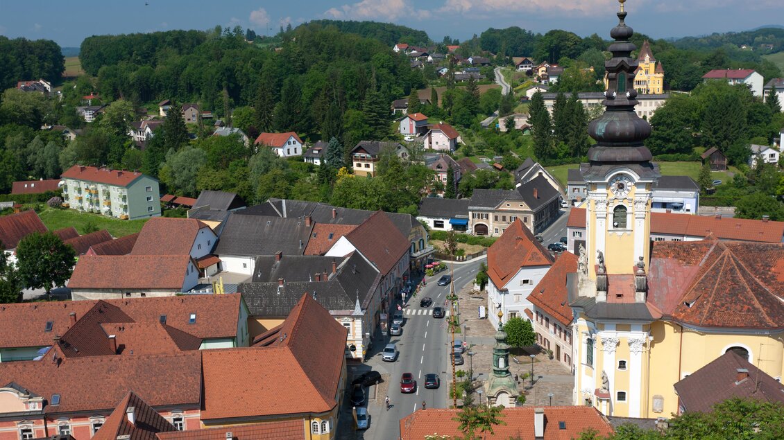Eine malerische Stadt mit roten Dächern und einer beeindruckenden Kirche. Im Hintergrund sind grüne Hügel und Bäume sichtbar. | © SYMBOL | SCHIFFER