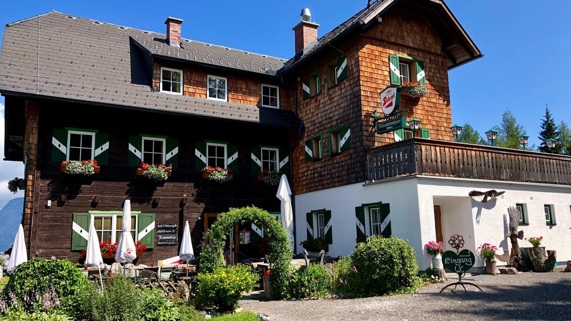 Ein charmantes Holzhaus mit Blumenfenstern und einem weißen Anbau. Der gepflegte Garten und die Sonnenschirme laden zum Verweilen ein. | © Michaelerberghaus