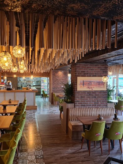 Ein modernes Restaurant mit Holzdekor und stilvollen Lampen. Die Einrichtung besteht aus grünen Stühlen und Holztischen. | © Milano Grande