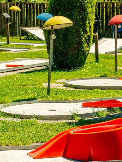 A mini golf course with colorful umbrellas and various play lanes. The green lawn and the sunny atmosphere invite you to play. | © Wolfgang Spekner