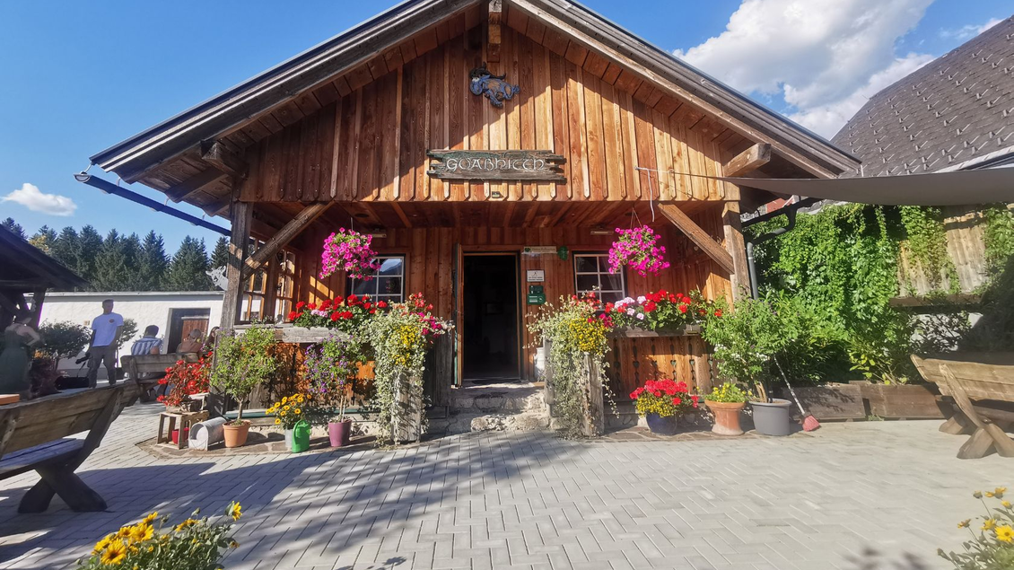 <p>Der Eingang in die Hütte mit bunten Blumen und Pflanzen im Vordergrund. Der Himmel ist blau mit einigen Wolken.</p> | © TVB Ausseerland Salzkammergut_Theresa Schwaiger