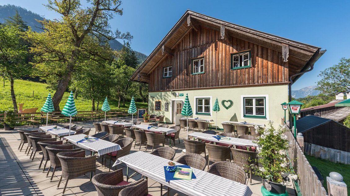 Ein gemütliches Restaurant mit einer Außenterrasse und Panoramablick auf die Natur. Grüne Sonnenschirme und Tischgedecke schaffen eine einladende Atmosphäre. | © Markus Mitterer