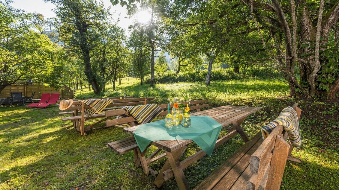 Ein gemütlicher Garten mit Holztischen und -bänken. Auf dem Tisch steht ein grünes Tuch mit einer Dekoration aus frischen Blumen und Getränken. | © Markus Mitterer