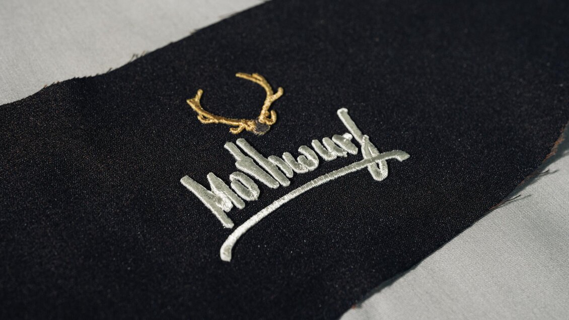 Gesticktes Mothwurf Firmenlabel mit weißem Schriftzug und goldenem Hirschgeweih auf dunklem Stoff. | © Bernd Grosseck