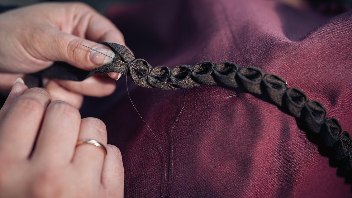 Eine handgefertigte Stoffverzierung wird bei Mothwurf mit Nadel und Faden von Hand an ein Kleidungsstück genäht. | © Bernd Grosseck