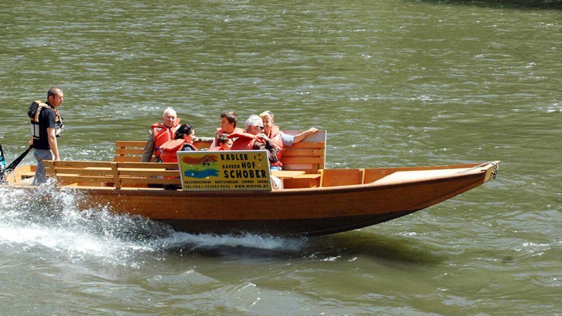 Ein Holzboot fährt auf einem Fluss. Die Passagiere genießen die Fahrt und tragen Schwimmwesten. | © Karl Schober