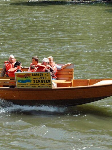 Ein Holzboot fährt auf einem Fluss. Die Passagiere genießen die Fahrt und tragen Schwimmwesten. | © Karl Schober