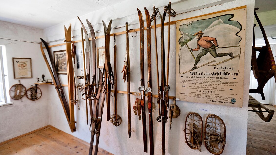 An einer Wand sind verschiedene alte Skier und Snowboards ausgestellt. Darüber hängt ein nostalgisches Plakat mit einem Ski-Fahrer. | © Holzwelt Murau