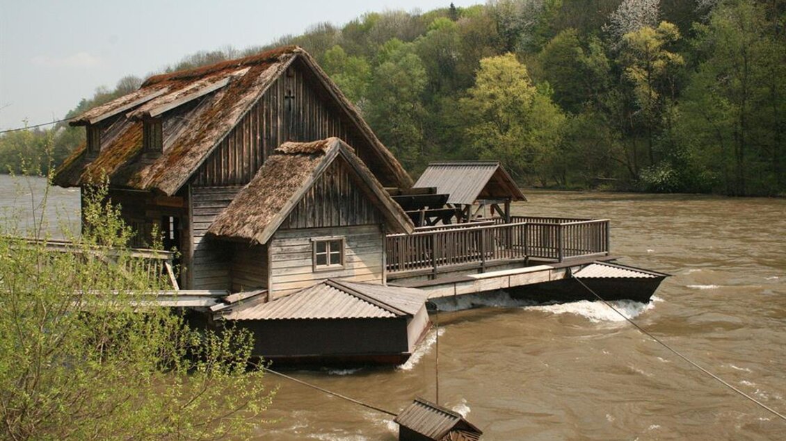 Ein charmantes Holzhaus am Fluss, umgeben von grünen Bäumen. Das Gebäude hat ein traditionelles Dach und eine kleine Veranda.