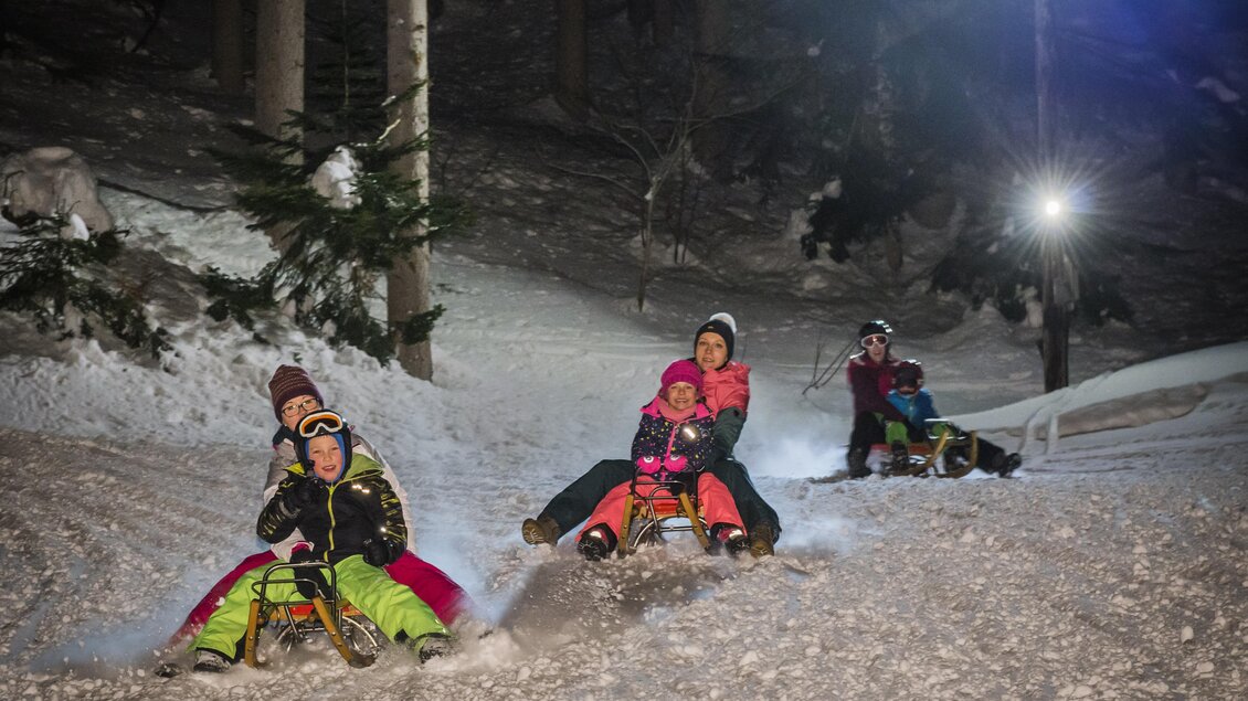 <p>Eine Gruppe von Menschen, die nachts die Piste bei der Grafenwiese in Tauplitz hinunterfahren. Die Atmosphäre ist fröhlich und winterlich und die Nachrodelbahn ist im Hintergrund beleuchtet.</p> | © Melanie Fritz