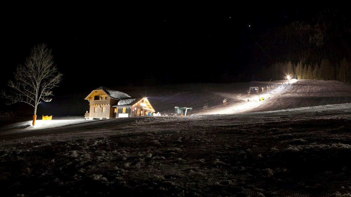 <p><p>Ein Schneebereich bei Nacht mit einem beleuchteten Skihang in Tauplitz. Im Hintergrund ist die Skihütte Grafenwiese zu sehen.</p></p> | © Nico Oussoren, Grafenwiese Tauplitz