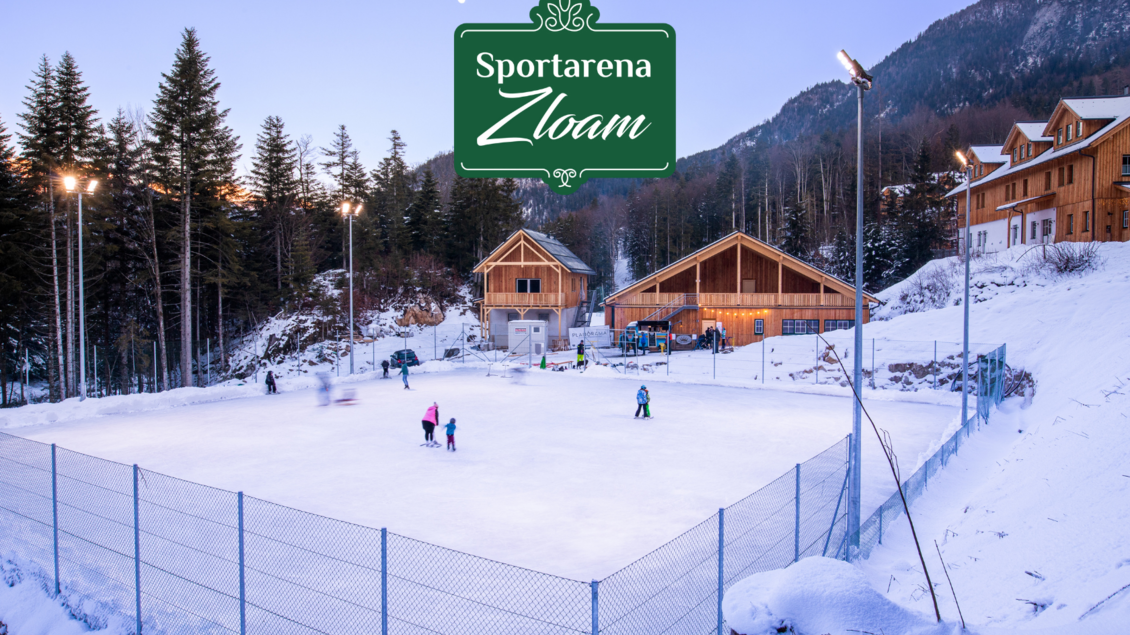 Eine idyllische Eislauffläche umgeben von schneebedeckten Bäumen und Hütten. Die Atmosphäre ist gemütlich und winterlich. | © www.zloam.at