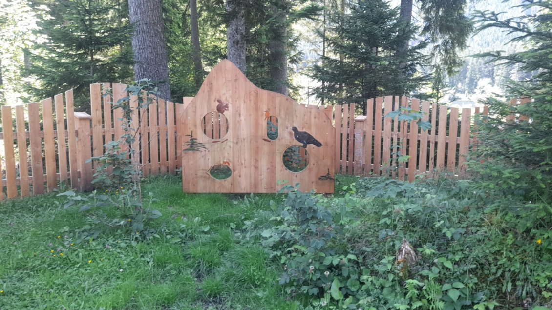 <p>Eine hölzerne Wand mit Tiermotiven des Waldes im Naturspielplatz am Ödensee, umgeben von einer grünen Wiese. Im Hintergrund stehen hohe Bäume.</p> | © Isabell Schachner
