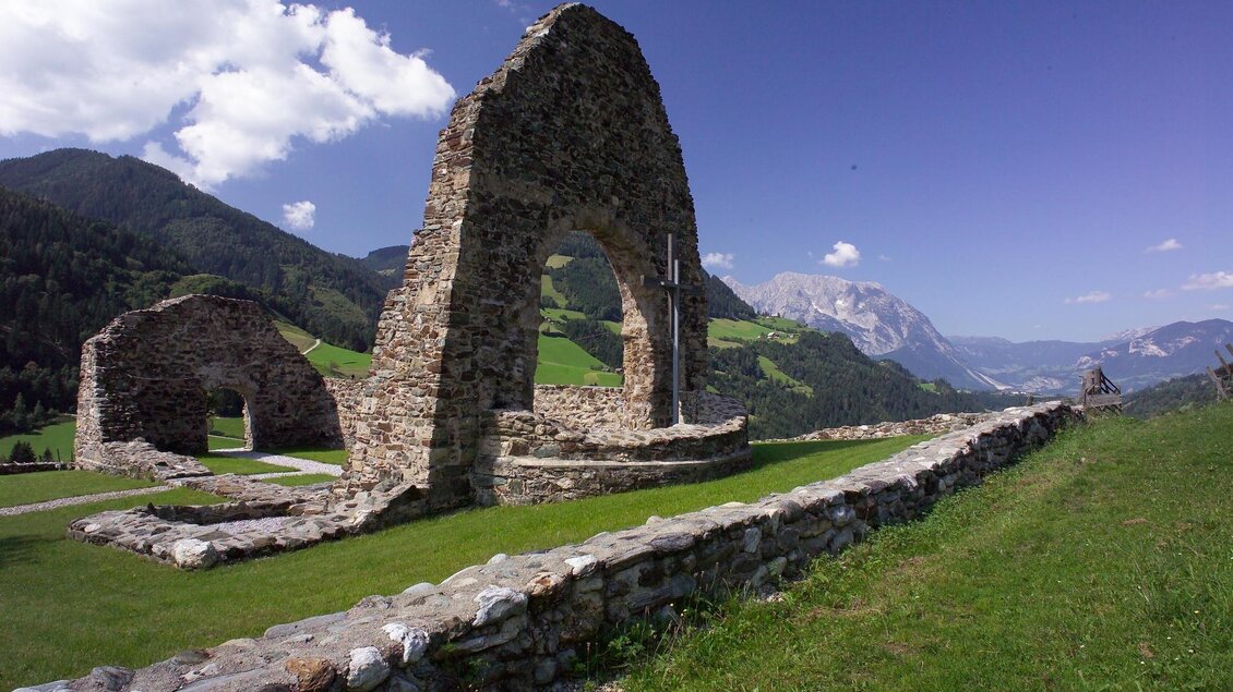 Die Überreste der historischen Ägydiuskirche stehen auf einer Anhöhe. Im Hintergrund sind bewaldete Berge und das Dachsteinmassiv unter blauem Himmel sichtbar. | © Hagspiel Photographie