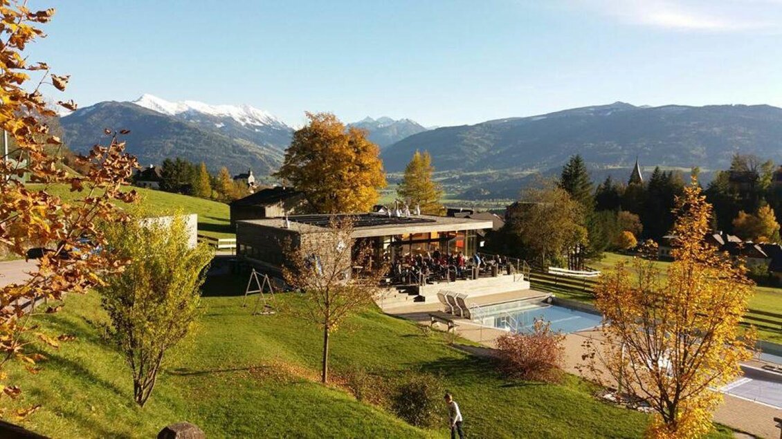 Ein modernes Gebäude in einer idyllischen Landschaft mit Blick auf schneebedeckte Berge. Der Außenbereich hat einen Swimmingpool und viele Bäume mit herbstlichen Farben. | © Naturbad Pürgg