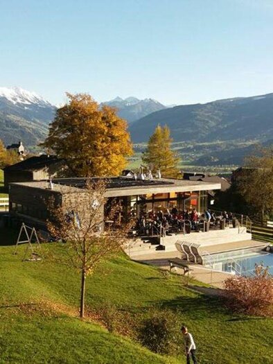 Ein modernes Gebäude in einer idyllischen Landschaft mit Blick auf schneebedeckte Berge. Der Außenbereich hat einen Swimmingpool und viele Bäume mit herbstlichen Farben. | © Naturbad Pürgg