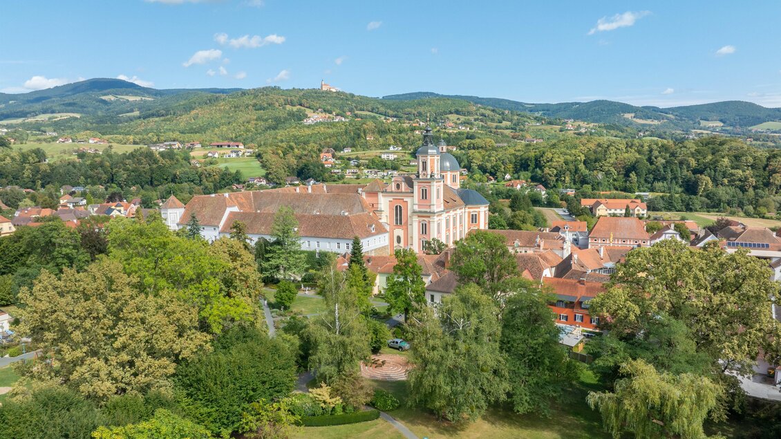 Eine malerische Stadt mit einer historischen Kirche und grünen Hügeln im Hintergrund. Die Umgebung ist von Bäumen und einer idyllischen Landschaft geprägt. | © Helmut Schweighofer