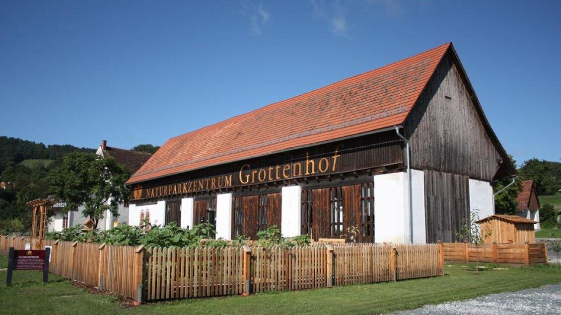 Ein charmantes Gebäude mit der Aufschrift "Naturparkzentrum Grottenhof". Vor dem Haus befindet sich ein geschmackvoll angelegter Garten mit Holzzäunen. | © Naturparkzentrum Grottenhof