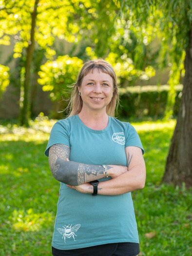 A smiling woman sits in front of a background with a green meadow. She is wearing a green T-shirt and appears friendly. | © Helmut Schweighofer