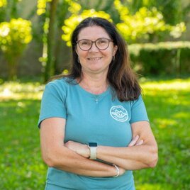 Eine lächelnde Frau sitzt vor einem Hintergrund mit einer grünen Wiese. Sie trägt ein grünes T-shirt und wirkt freundlich. | © Helmut Schweighofer