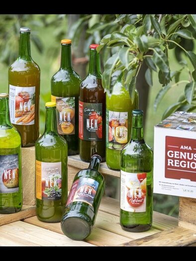 A selection of different bottles with drinks is placed on a wooden palette. In the background, green plants can be seen, creating a fruity atmosphere. | © Treichler