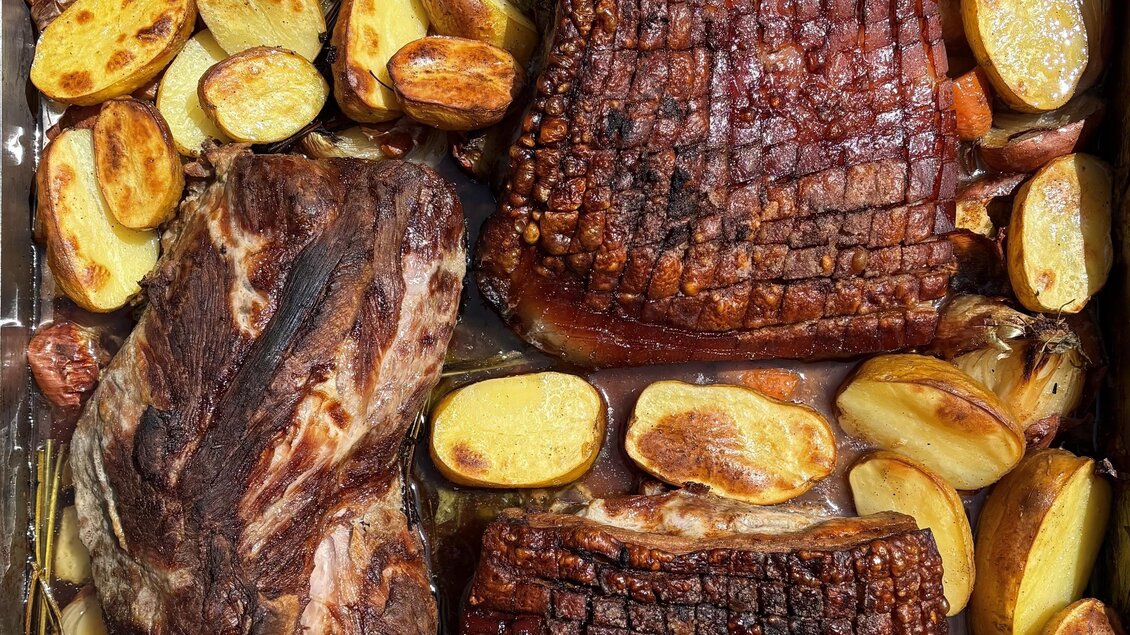 Ein köstliches Gericht mit mehreren Fleischstücken, die goldbraun gebraten sind. Rundherum liegen halbierte Kartoffeln, die ebenfalls gebräunt sind.