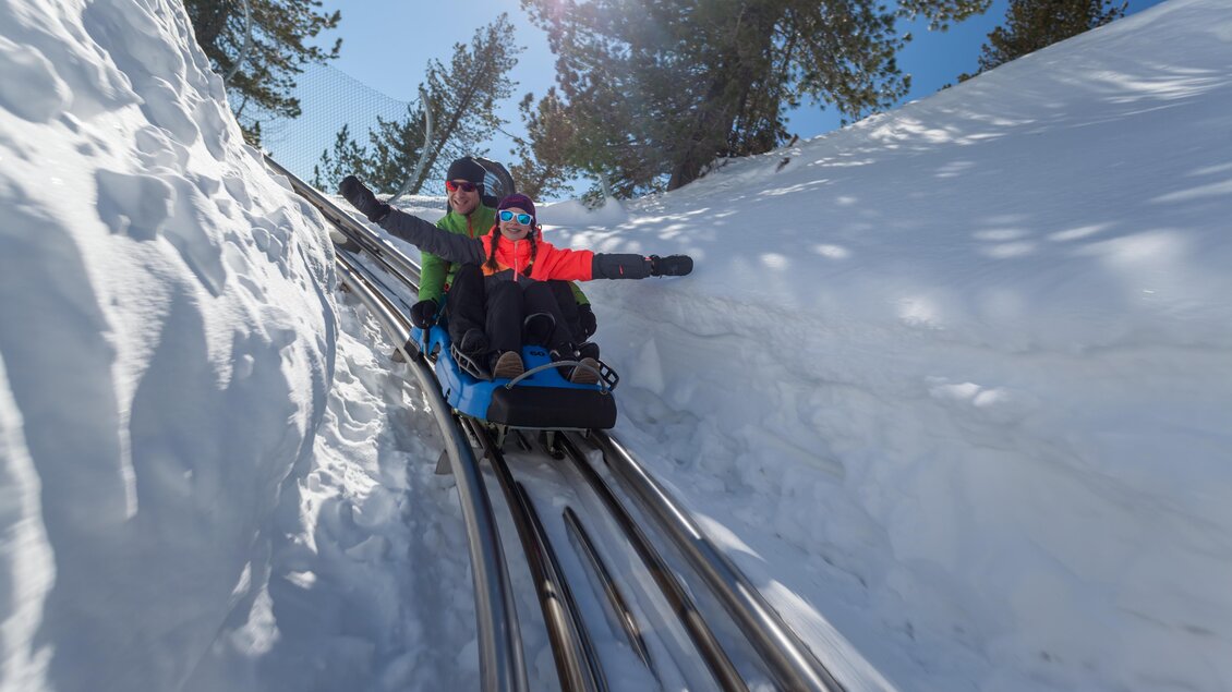 Eine aufregende Abfahrt auf einer Rodelbahn im Schnee. Die beiden Fahrer genießen die Fahrt unter einem klaren Himmel. | © TMG Turracher Höhe Marketing GmbH