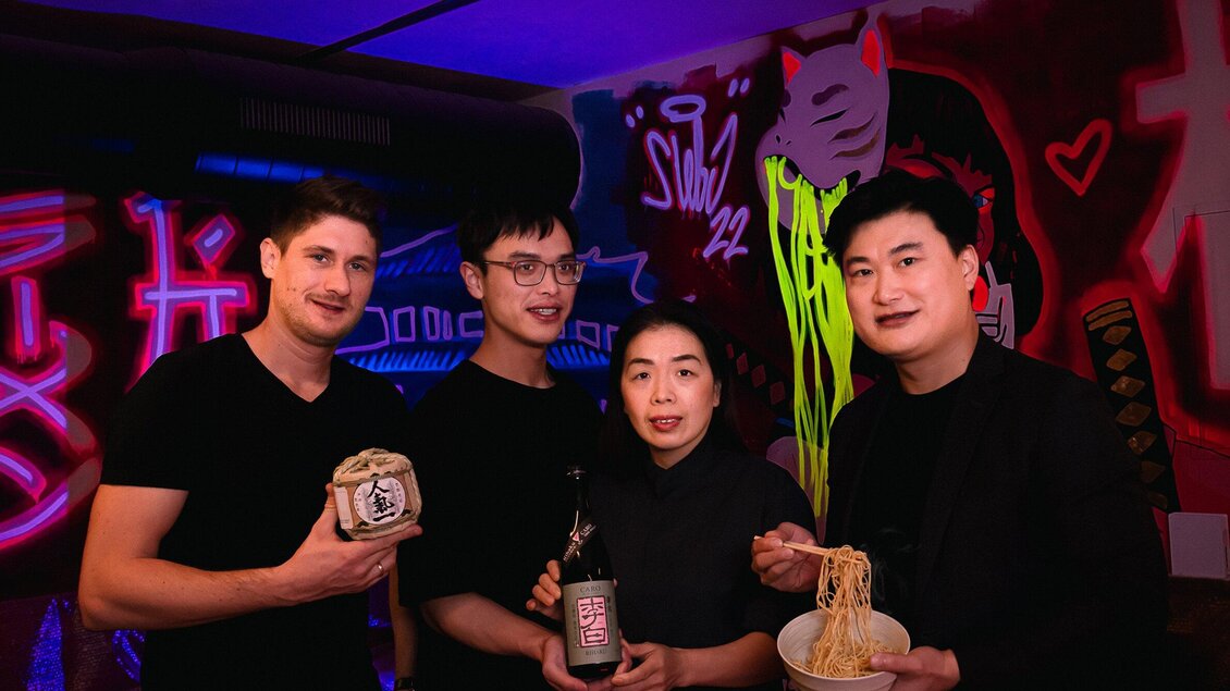 Eine Gruppe von vier Personen steht in einem bunten Raum mit Graffiti. Sie halten verschiedene Speisen und Getränke in der Hand. | © Noonbar - Moriwano Group