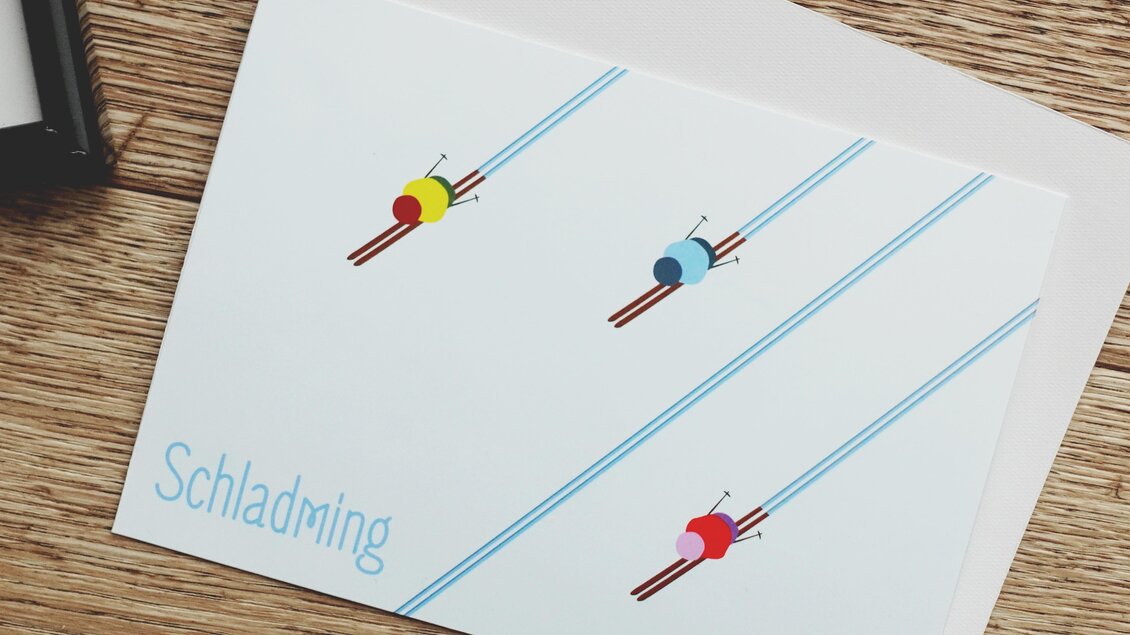 Eine minimalistisches Design mit drei Skifahrern auf einer weißen Karte. Die Aufschrift „Schladming“ und die blauen Linien symbolisieren die Skipiste.