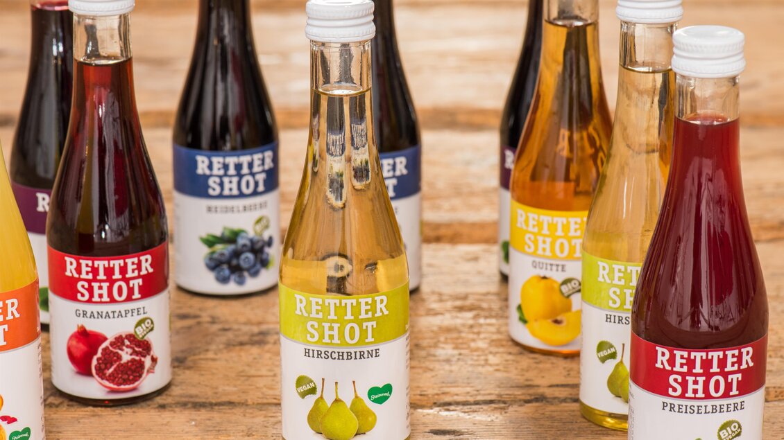 Verschiedene Flaschen von „Retter Shot“ stehen auf einem Holztisch. Die Flaschen haben unterschiedliche Farben und Geschmäcker wie Granatapfel, Birne und Himbeere. | © Helmut Schweighofer