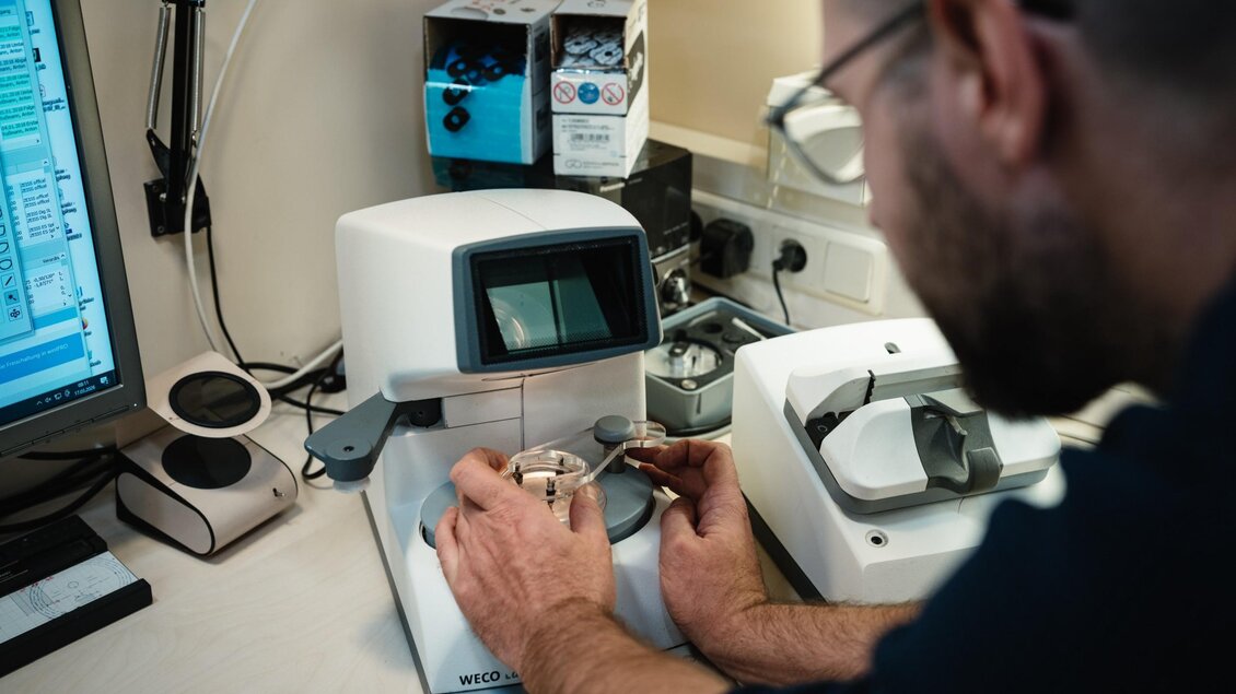 Optiker bearbeitet ein Brillenglas an einem Präzisionsgerät bei Optik Rossmann in Graz. | © Bernd Grosseck