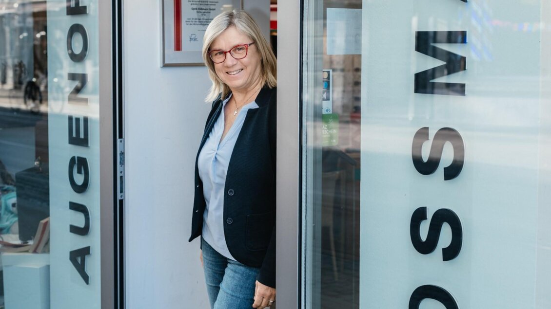 Inhaberin von Optik Rossmann mit roter Brille im Eingang des Optikgeschäfts in Graz. | © Bernd Grosseck