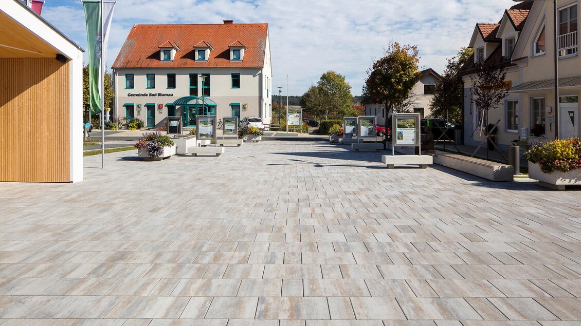 Ein ruhiger Platz mit modernen Pflastersteinen. Im Hintergrund sieht man gepflegte Gebäude und einen klaren Himmel. | © Gemeinde Bad Blumau/Markus Kaiser