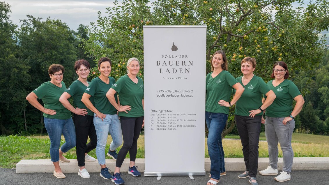 Eine Gruppe von Frauen steht in grünen T-Shirts vor einem Banner des Pollauer Bauernladens. Im Hintergrund ist eine grüne Landschaft mit Bäumen zu sehen. | © Bauernladen Pöllau