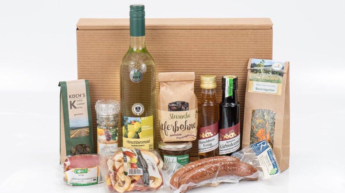 Ein Geschenkkorb mit verschiedenen Lebensmitteln, darunter Wein, Honig, Wurst und Tee. Die Artikel sind ansprechend angeordnet und stehen auf einem weißen Hintergrund. | © Bauernladen Pöllau