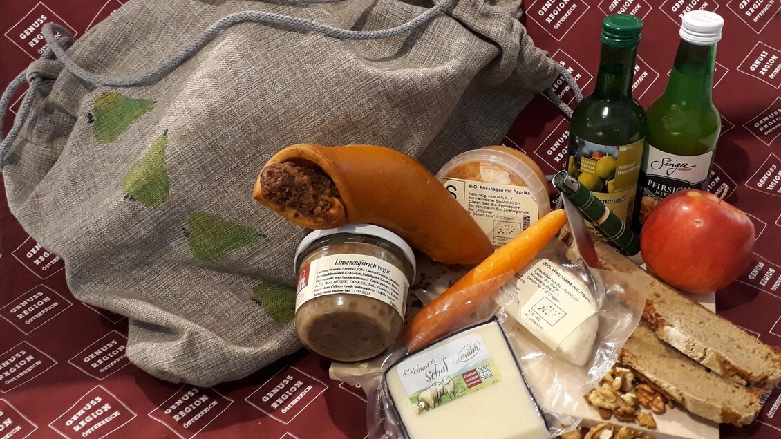 Eine Stofftasche voll mit verschiedenen Lebensmitteln, darunter Käse, Aufstrich, Obst und Gemüse. Dazu gehören auch Flaschen mit Getränken und ein paar Nüsse. | © Katharina Grasser