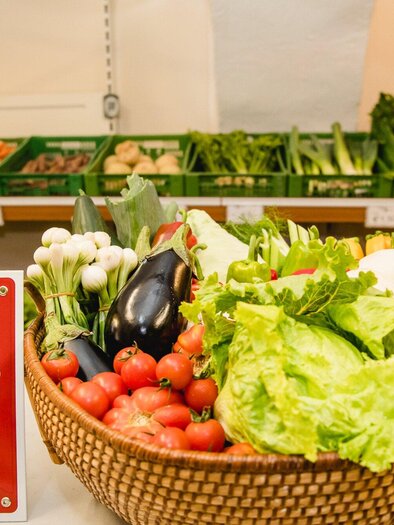 A basket of fresh vegetables is on a table. In the background, green boxes with more vegetable products can be seen. | © AMA GENUSS REGION - Mias Photoart