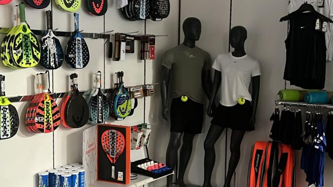 Ein Sportgeschäft mit verschiedenen Rackets und Sportbekleidung. Die Wände sind mit Accessoires und Kleidung ausgestattet, während mehrere Mannequins die Outfits präsentieren.