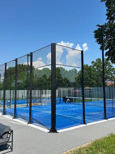 Ein moderner Padelplatz mit blauen Spielflächen und hohen Netzwänden. Im Hintergrund sind grüne Bäume und ein klarer Himmel zu sehen. | © Freibad Frauental (c) Florian Pacher