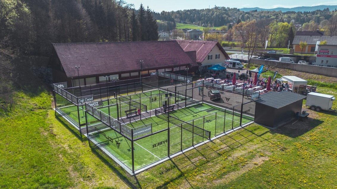 Ein moderner Sportplatz mit mehreren Padel-Tennisplätzen und einer angrenzenden Sporteinrichtung. Die Anlage liegt in einer grünen Umgebung, umgeben von Bäumen und Hügeln. | © Padelbase Wies
