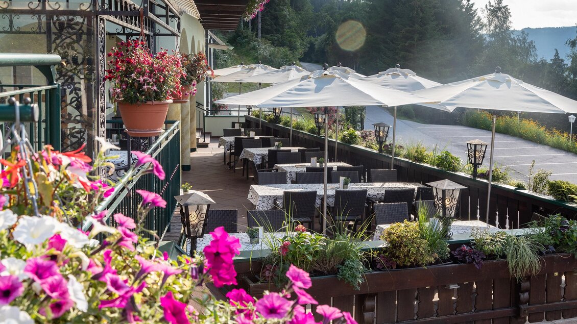 Eine gemütliche Restaurantterrasse mit Tischen und Sonnenschirmen. Bunte Blumen verschönern die Umgebung und laden zum Verweilen ein. | © Panoramahotel Gürtl